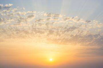 bright yellow-orange sunset over the sea against a blue sky with multicolored pink clouds and sun rays all over the sky
