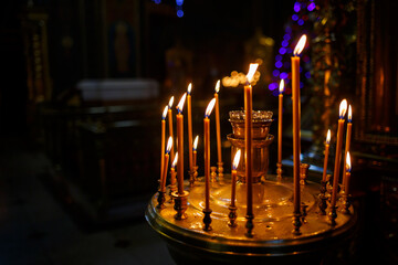 Many burning candles stand in a golden stand in the church