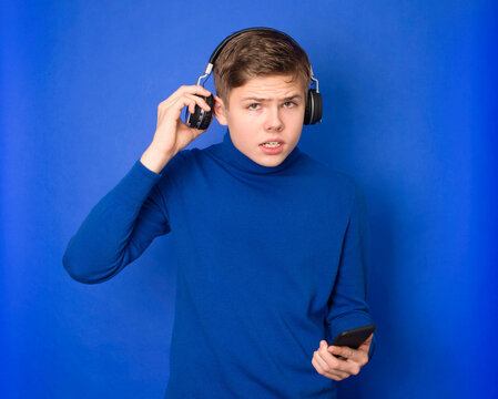 Tenager boy listening music with headphones from a smart phone and asks what?