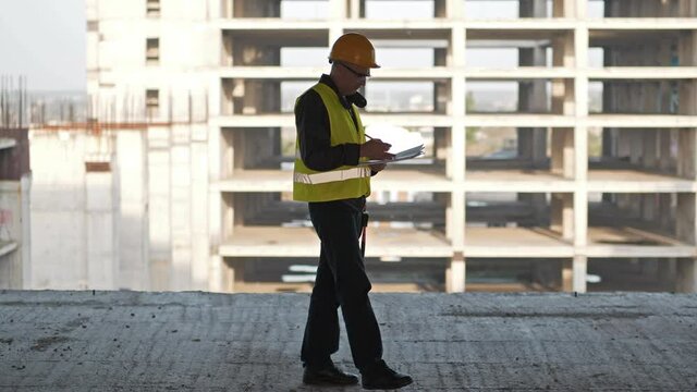 Onsite foreman walks on construction site, holds in hands project documentation and takes notes in them. 4K 60fps panoramic video