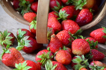 Ripe strawberries with leaves in wicker basket on wooden table on blurred background