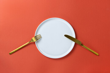 Fototapeta na wymiar Fashionable blank white round plate with golden cutlery on red paper, minimal style flat lay, copy space. Mockup for restaurant, cafe, delivery service, social media. Concept Valentine's day food