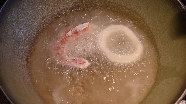Home life scene: close-up footage of floured shrimps and squid rings being dipped in hot oil. Hot oil in contact with food immediately begins to fry. They are then turned with a fork.