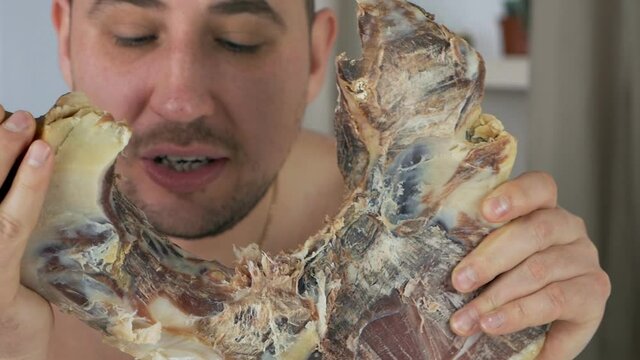The bald man is disgusting, gnawing Spanish serrano ham on the bone in his apartment