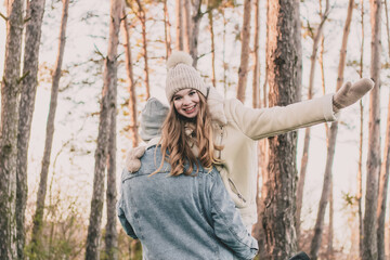 
The guy carries the girl on his shoulder and she smiles against the background of a pine forest