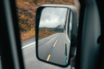 View from side mirror of camper van or rental car. Reflection of beautiful mountain road in autumn...