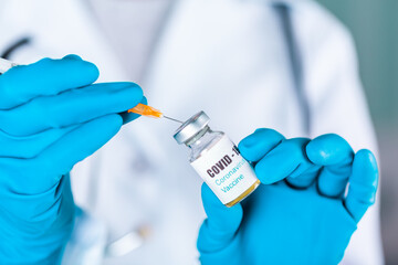 Woman doctor or nurse in uniform and gloves wearing face mask protective in lab holding medicine vial vaccine bottle with COVID-19 Coronovirus vaccine label