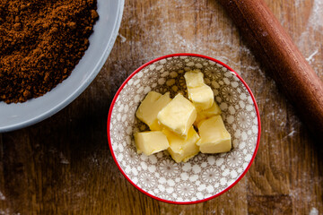 Bowl of cubed butter on a wooden background with a bowl of brown sugar next to it