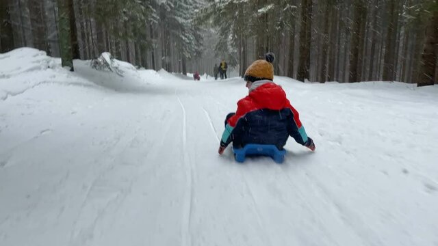 Happy children, going down the slope on a plastic sledge, speeding, happiness