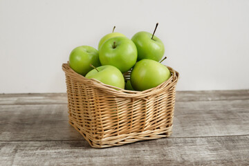 green apples in a wicker basket on a wooden table