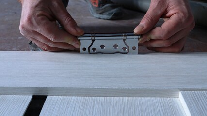 installation of door fittings made of shiny metal close-up, fixation of door hinges in the process...