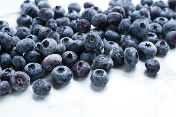 Tasty frozen blueberries on white marble table, closeup