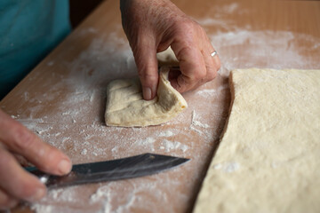 Grandmother's hands cut with a knife raw homemade dough for baking. Side view.