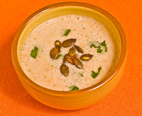 top view, close distance of a ceramic bowl of freshly prepared, homemade pumpkin and turkey soup, with toasted pumpkin seeds and parsley, on an orange place mat