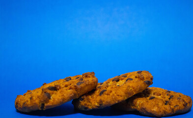 Three oat biscuits with a crumb of chocolate on a blue background