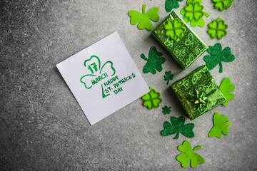 Decorative clover leaves, green gifts box, coins on stone background, flat lay. St. Patrick's Day...