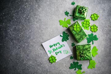 Decorative clover leaves, green gifts box, coins on stone background, flat lay. St. Patrick's Day...