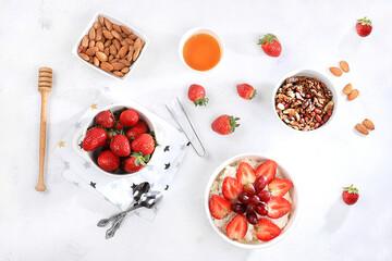 Useful breakfast with ingredients, strawberry yogurt with muesli, grapes and honey on a bright table, fruit salad. Healthy and natural food concept, lifestyle, food for children, selective focus