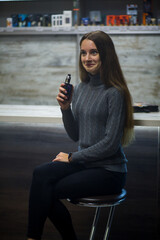 Fototapeta premium Vaping teenager. Young pretty white caucasian teenage girl with long hair smoking an electronic cigarette indoors. Deadly bad habit. Vape activity.