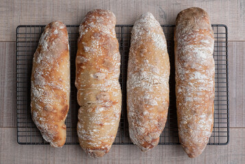 Home made ciabatta sour dough loaves cooling on wire tray on wooden surface, baked during the Coronavirus lockdown.