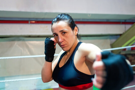 Female boxer ready to kick with black boxing bandage on hands in gym.