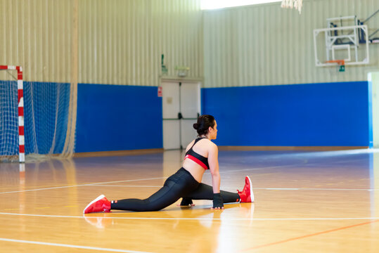 Female fighter in sportswear doing stretching, sitting on floor at gym