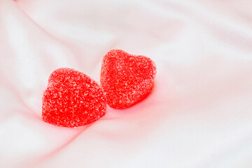 Two red heart shaped gummy candies on silk background
