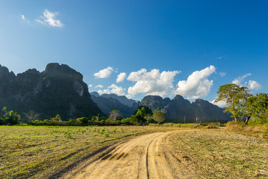 Dirt road in farm with limestone mountains in background, Vang Vieng, Laos
