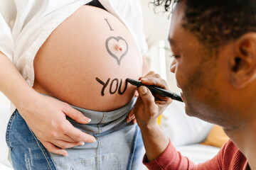 Husband drawing the phrase I love you on the belly of his pregnant wife. Parenthood concept