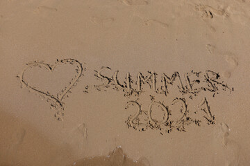 Inscription SUMMER 2021 is written on wet sand. Tourist summer season 2021 concept