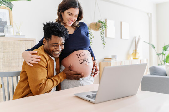 Husband and pregnant wife celebrating ultrasound results in front of a laptop, with a phrase written on her belly that it is a girl. Parenthood concept