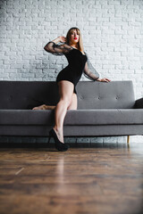 Fototapeta premium Young sexy blonde with naked legs in high heel shoes posing near the sofa