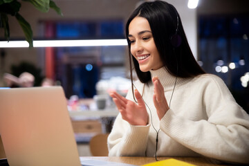 Smiling young female in headphones with laptop applaud watching webinar or communicate by conference video call