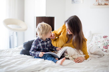 Mother, toddler child and puppy dog, lying on the bed, reading book together, family time