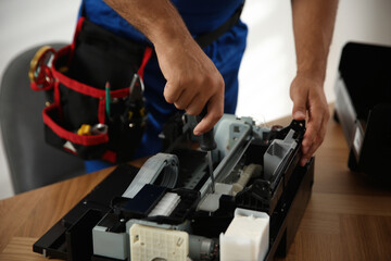 Repairman with screwdriver fixing modern printer indoors, closeup