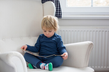 Mother and child, toddler boy, reading a book, sitting in a cozy armchair