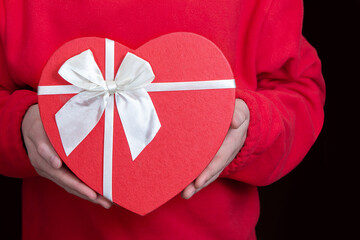 Red gift box in the shape of a heart in hands. Valentine's Day. A gift for your beloved on February...