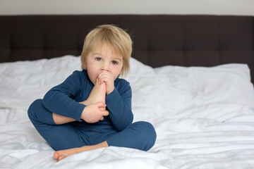Cute blond toddler child, sucking his foot thumb, making funny faces