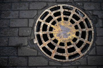 A rusty sewer manhole with holes in the road.