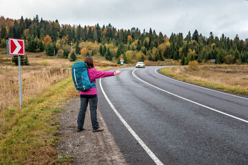 Fototapeta premium Travel woman backpacking hitchhiking on road trip, hitching a ride from car