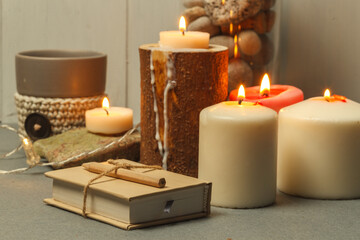 Burning thick white candles on the table, a cup of coffee and a sketchbook. Close-up