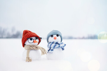 Festive background with a lovely snowman. Christmas card with two little snowmen the girl and the boy in knitted caps and scarfs on snow in the winter, copy space. 