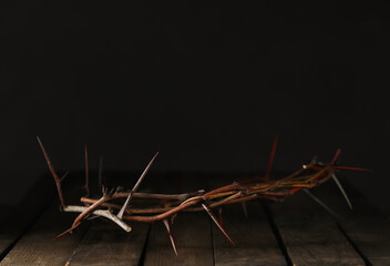 Crown of thorns on wooden table against dark background, space for text. Easter attribute