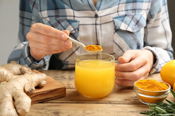 Woman adding turmeric to immunity boosting drink at wooden table with ingredients, closeup - obrazy, fototapety, plakaty