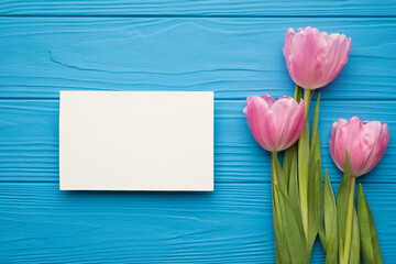 Photo of three beautiful tulips on green stems with blank empty paper card with space for design isolated bright color blue backdrop