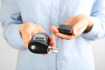 Woman holding modern breathalyzer and car key on light background, closeup