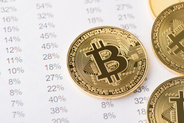 Photo of golden shiny bitcoin laying on numbers with percentage ont he backgroundAbove top close up view photo of golden shiny bitcoin laying on numbers with percentage ont he background