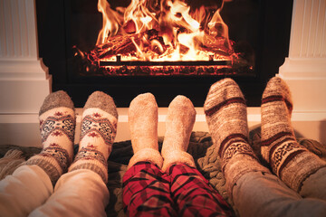 Lovely family in warm socks resting near fireplace at home, closeup