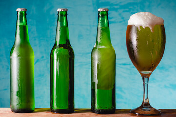 Tres botellas verdes con cerveza, un vaso de cerveza con espuma, sobre fondo azul.