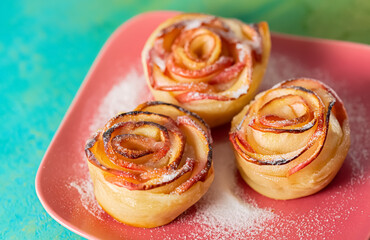 Pieces of apples baked and sprinkled with sugar on a square pink plate. Flower with apples. Soft focus